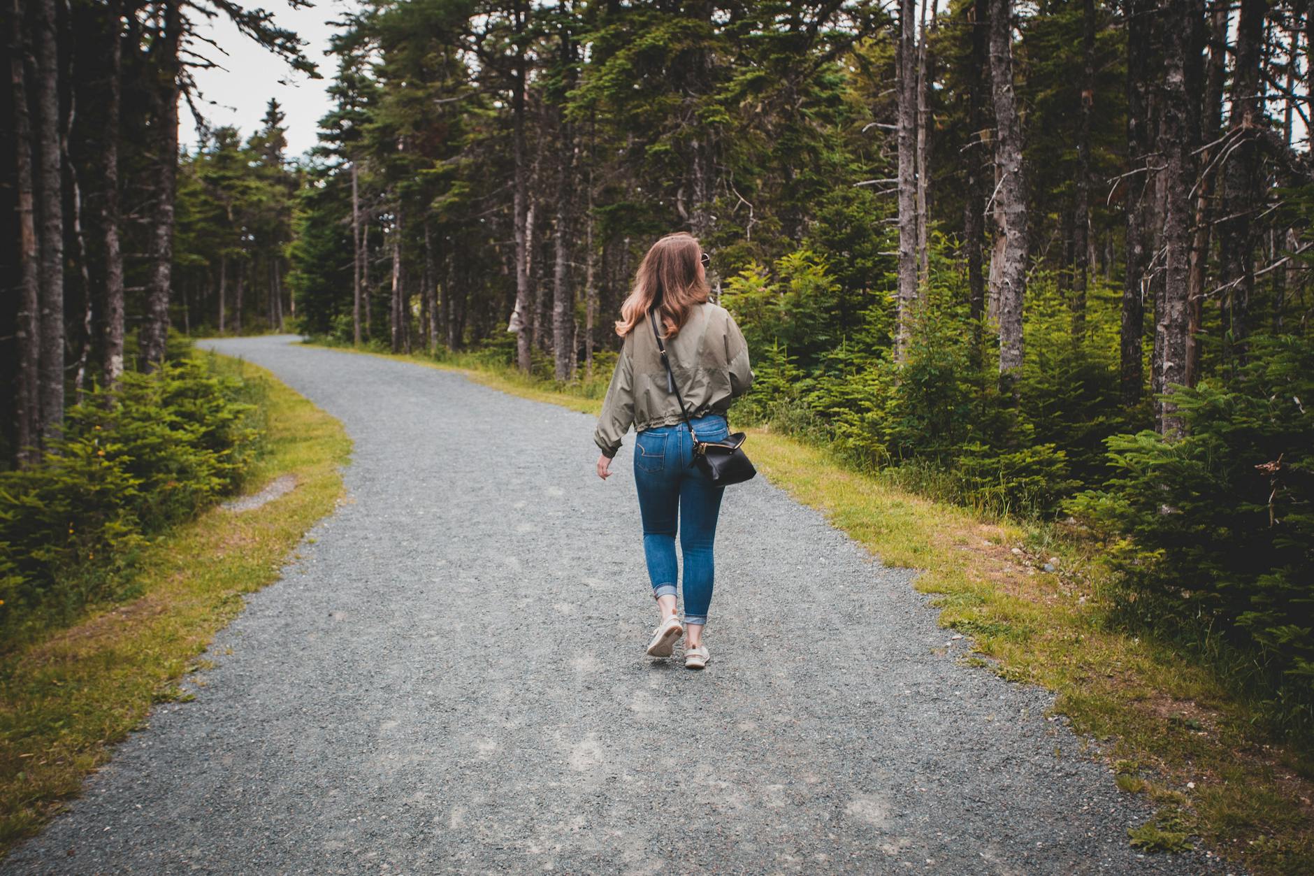 Młoda kobieta spaceruje letnią leśną ścieżką wśród zieleni