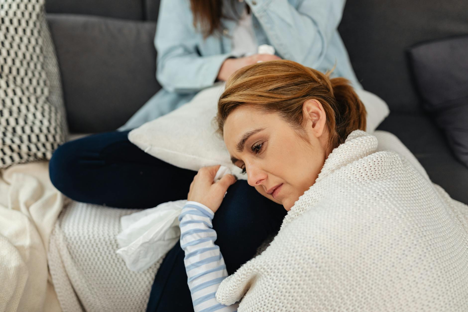 Zamknięta w koc kobieta zamyślona na kanapie, wygląda na przygnębioną